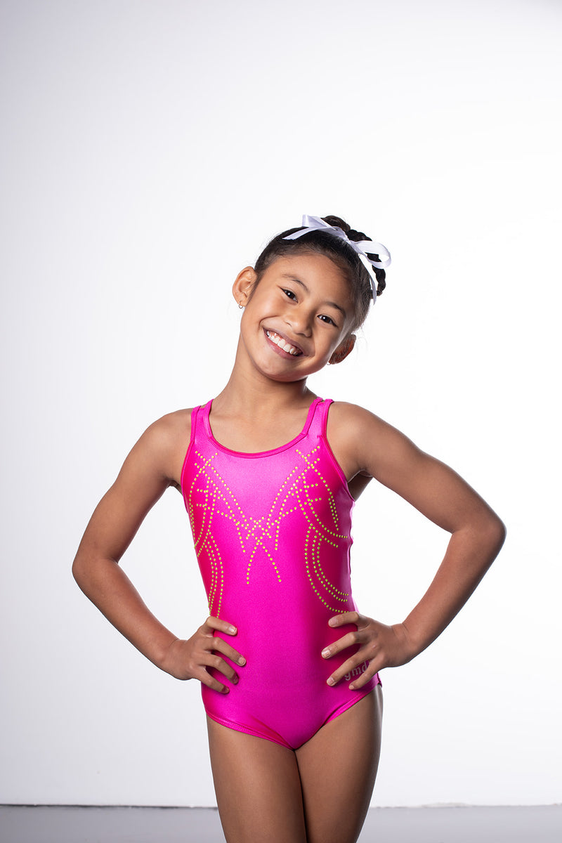Photo of a 10 year old girl infront of a white background wearing a bright hot pink sheen leotard. The front features jelly yellow crystals, and the back has 4 thin straps twisted through a gathered back opening creating a traingle. 