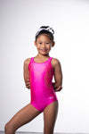Photo of a 10 year old girl infront of a white background wearing a bright hot pink sheen leotard. The front features jelly yellow crystals, and the back has 4 thin straps twisted through a gathered back opening creating a traingle. 