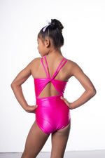 Photo of a 10 year old girl infront of a white background wearing a bright hot pink sheen leotard. The front features jelly yellow crystals, and the back has 4 thin straps twisted through a gathered back opening creating a traingle. 