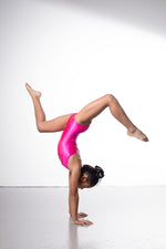 Photo of a 10 year old girl infront of a white background wearing a bright hot pink sheen leotard. The front features jelly yellow crystals, and the back has 4 thin straps twisted through a gathered back opening creating a traingle. 