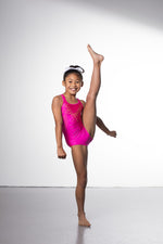 Photo of a 10 year old girl infront of a white background wearing a bright hot pink sheen leotard. The front features jelly yellow crystals, and the back has 4 thin straps twisted through a gathered back opening creating a traingle. 