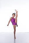 Photo of a 10 year old girl standing infront of a white background. Wearing a short sleeve plum coloured gymnastics leotard. The top of the leotard is a shiny plum fabric, and the lower is a matte plum fabric. The matte fabric has a heavy amount of crystal detailing, to make it very sparkly. 