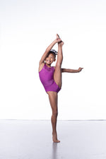 Photo of a 10 year old girl standing infront of a white background. Wearing a short sleeve plum coloured gymnastics leotard. The top of the leotard is a shiny plum fabric, and the lower is a matte plum fabric. The matte fabric has a heavy amount of crystal detailing, to make it very sparkly. 
