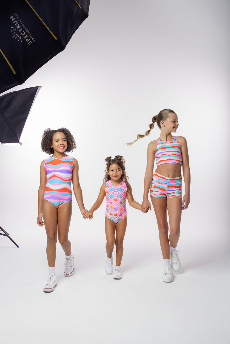 Photo of a 5 year old girl, standing iPhoto of a 10 year old girl standing infront of a white backdrop. Wearing a wavy pattern gymnastics leotard that is a mix of purple, aqua, white & purple. There are no crystals, making it great for training.