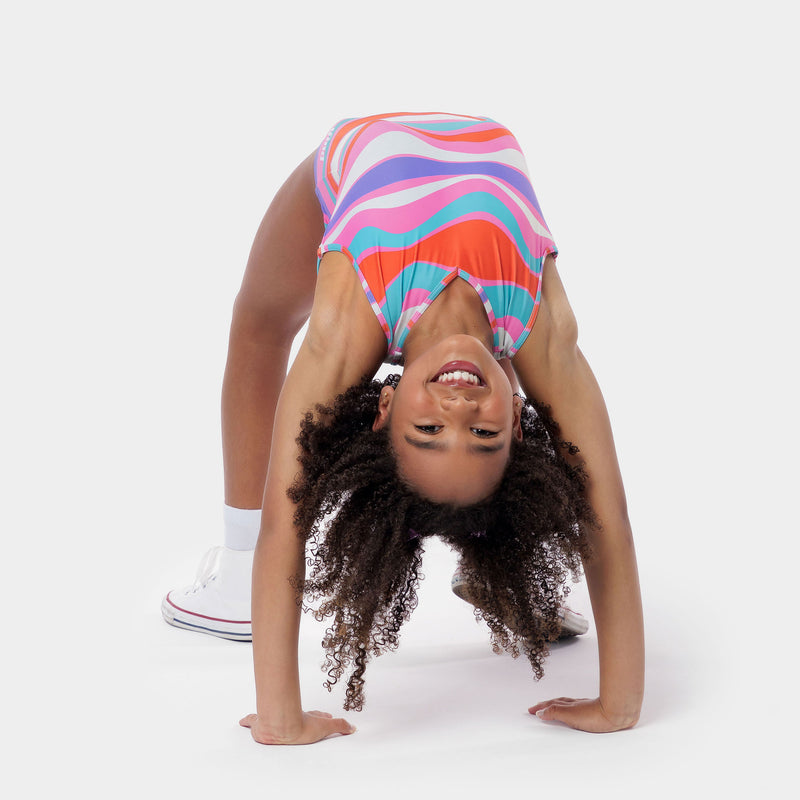 Photo of a 5 year old girl, standing iPhoto of a 10 year old girl standing infront of a white backdrop. Wearing a wavy pattern gymnastics leotard that is a mix of purple, aqua, white & purple. There are no crystals, making it great for training.