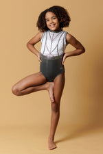 Girl staning infront of a beige background, wearing a white & gunmetal grey gymnastics leotard. The top half of the letoard is white and is not see through. It is encrusted with crystals and features gunmetal grey shiny applique detailing. The lower half is shiny gunmetal mystique fabric. Fully lined.