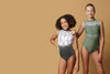Girl staning infront of a beige background, wearing a white & gunmetal grey gymnastics leotard. The top half of the letoard is white and is not see through. It is encrusted with crystals and features gunmetal grey shiny applique detailing. The lower half is shiny gunmetal mystique fabric. Fully lined.