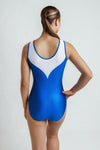 girl standing infront of a white background, weaing a rich royal blue leotard. The leotard has slight sheen, and has a white mesh panel at the top. It has AB crystals on the front & back in a waterfall pattern.