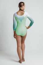 Girl standing on a white background wearing a lime green 3/4 sleeve leotard with lots of crystals. The top of the leotard is white, then fades into a green a the base of the sleeve.