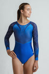 Photo of a girl infront of a grey backdrop, wearing a long sleeve gymnastics competition leotard. The leotard is a mixture of royal blue & navy blue. The royal blue lower gives off a nice sheen, and the upper is an ombre from light to dark with lots of crystal detailing. The sleeves are long with heavy two colour crystal detailing in a criss cross pattern. Extremely sparkly leotard. 