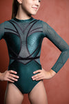 Photo of a 12 year old girl standing infront of a terracotta backdrop. Wearing a deep Green and black Girls Gymnastics long sleeve WAG Competition Leotard by GMD Activewear Australia. 